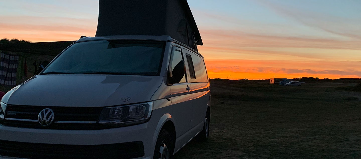 VW Bulli vor einem Sonnenuntergang an der Küste in Frankreich
